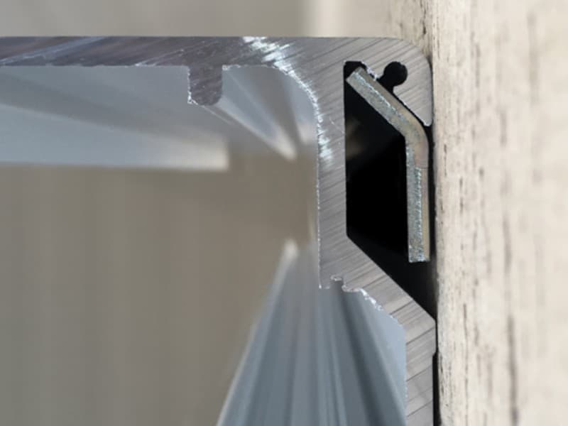 Cross-sectional view of an aluminium track profile used in automatic sliding door systems, mounted against a wall, showing internal guide channels and mounting grooves.