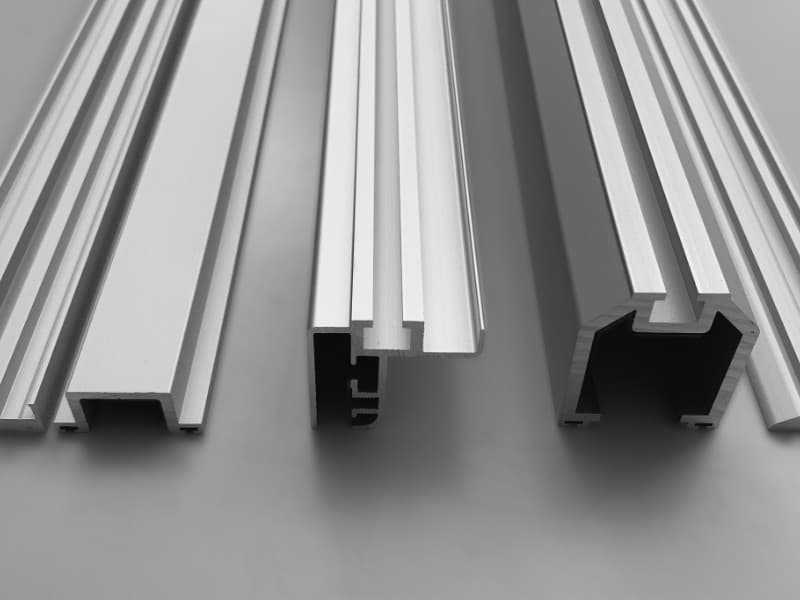 Assorted aluminium profiles for automatic sliding door systems, displayed upright to show various cross-sectional designs used for tracks, frames, and enclosures.