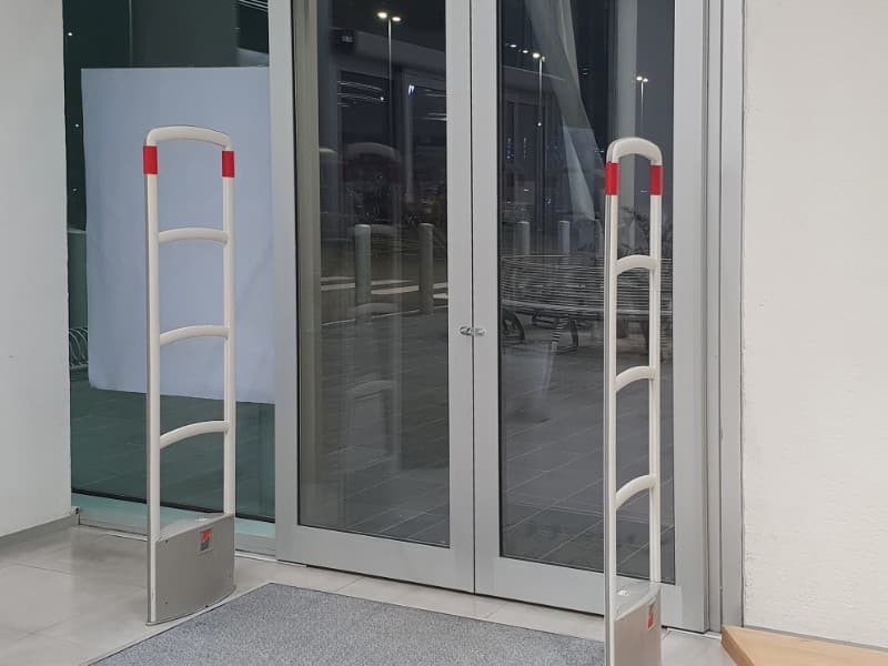 Glass entrance doors in a retail store fitted with anti-theft security sensors on either side, providing access control while maintaining visibility to the outside.