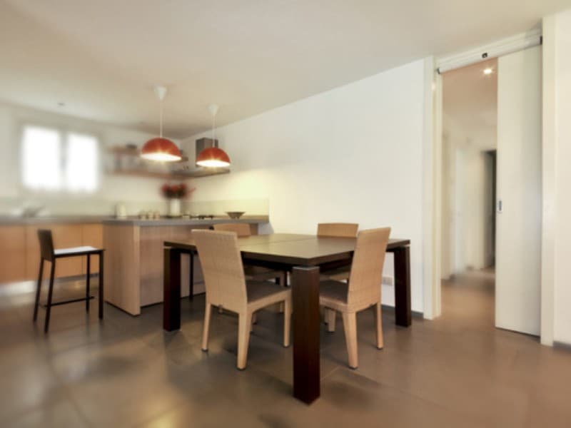 Modern dining area with a kitchen in the background and a white automatic sliding pocket door partially open, leading to a hallway.