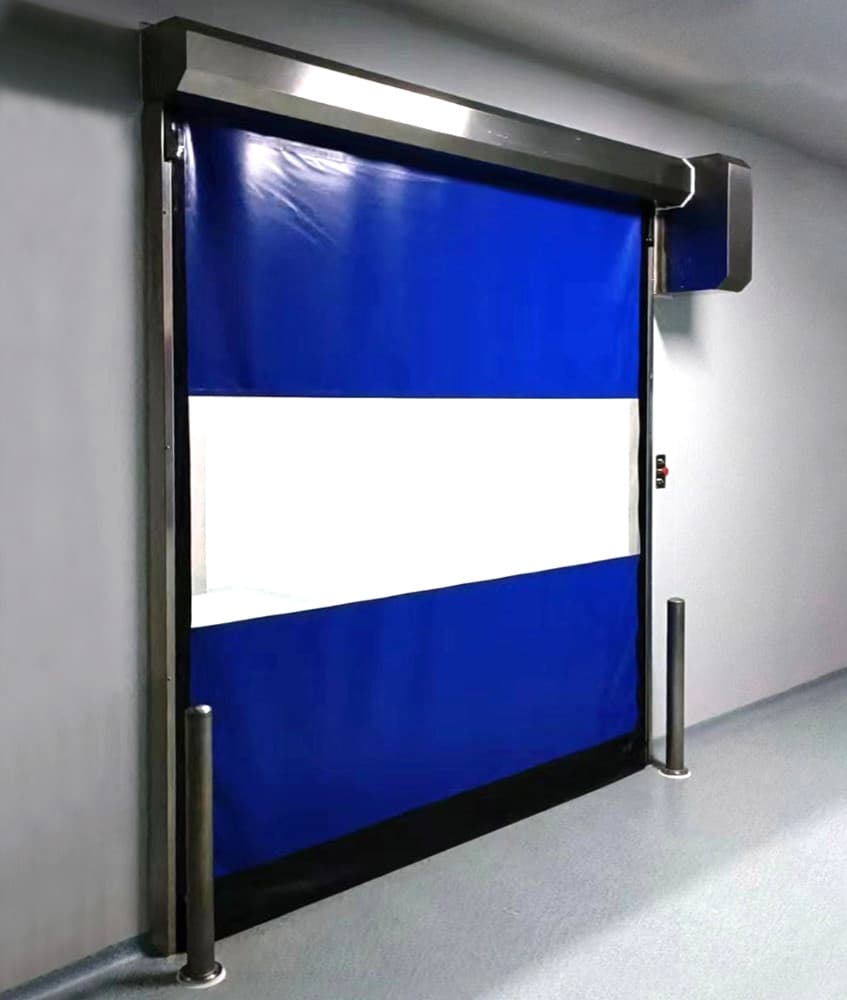 Photo of a blue high-speed door with a white transparent vision panel in the middle, featuring stainless steel side posts and a sleek header design. The door is installed in a clean, modern corridor with light grey flooring.