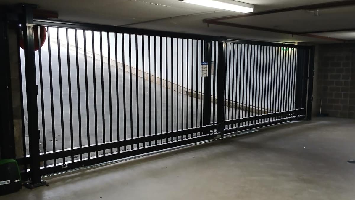 Black sliding gate securing basement car park entrance of an apartment building.