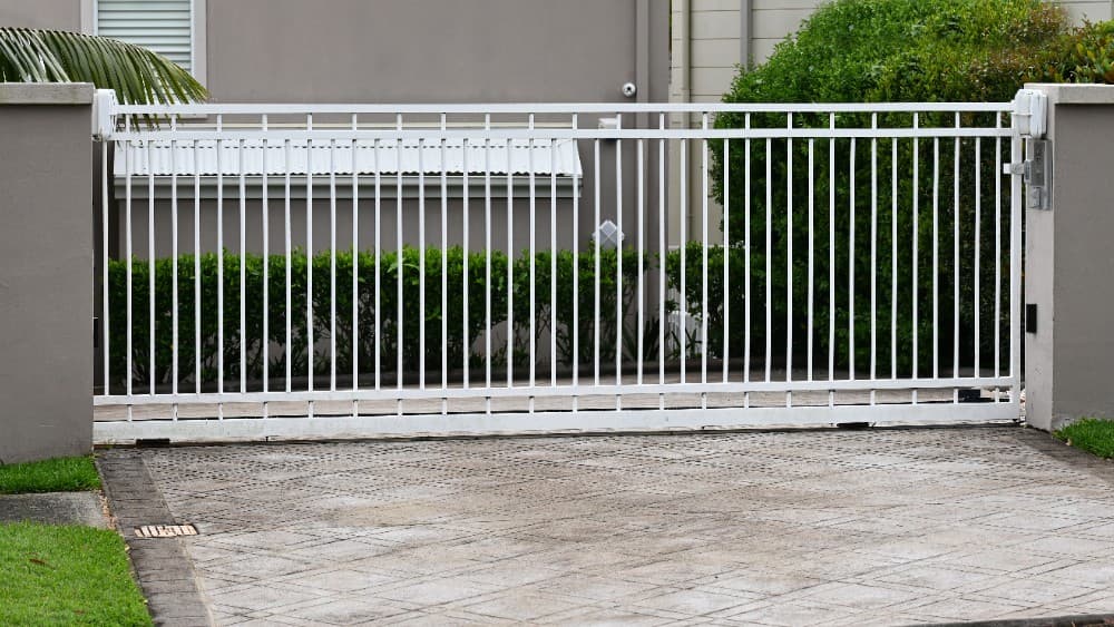 White steel sliding gate installed at a suburban residential driveway.
