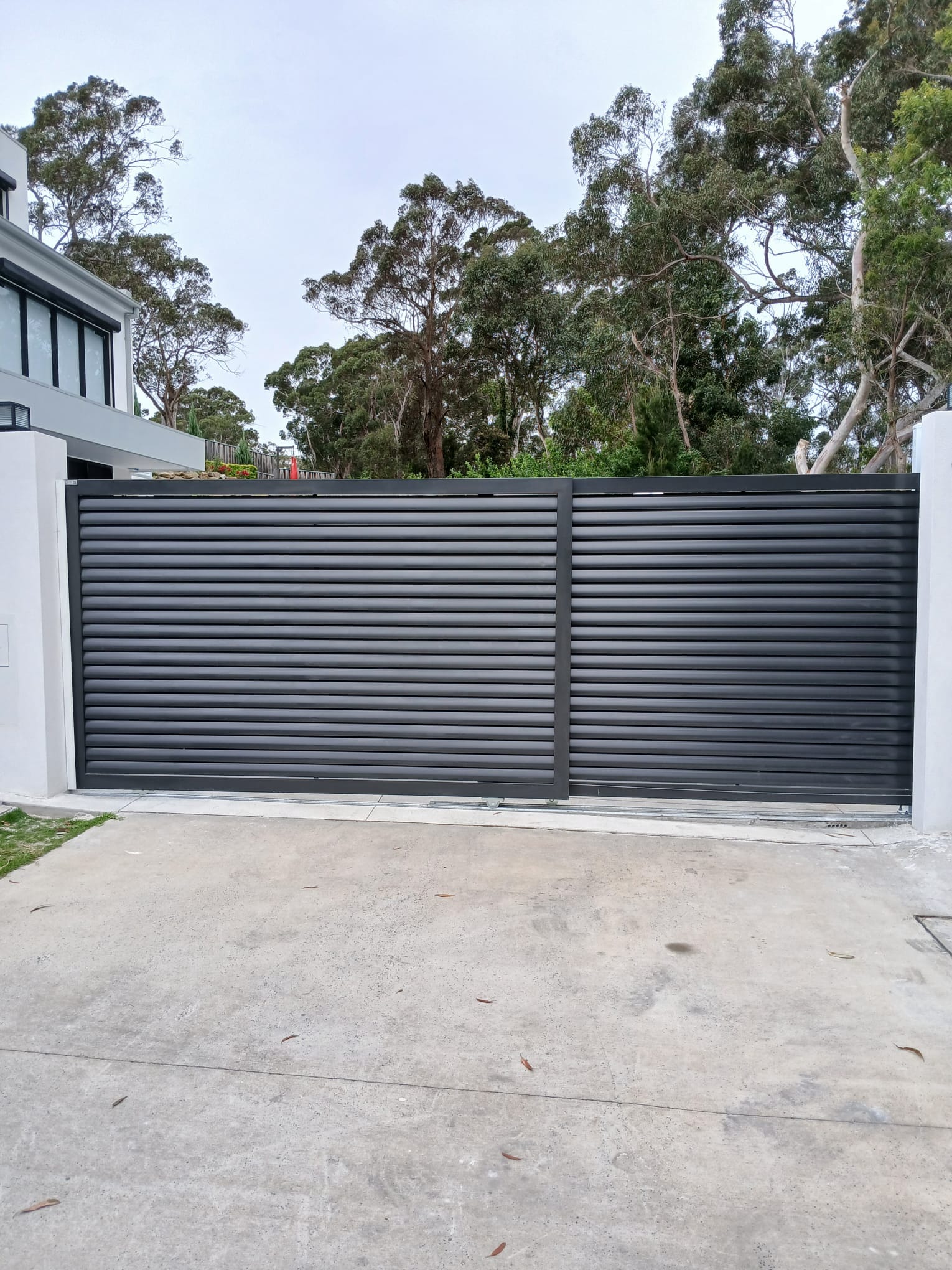 Completed charcoal horizontal-slat automatic sliding gate across a residential driveway.